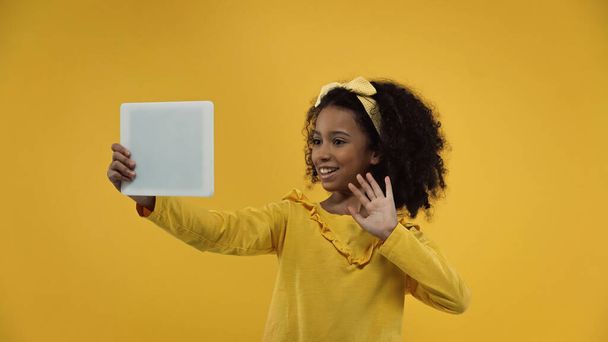 szczęśliwy Afryki dziewczyna macha ręką podczas mając wideo połączenie na cyfrowy tablet odizolowany na żółty - Zdjęcie, obraz