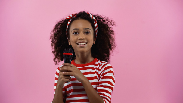 vrolijk afrikaans amerikaans meisje holding microfoon geïsoleerd op roze - Foto, afbeelding