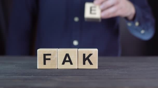 Een man in een shirt componeert het woord FAKE uit houten blokjes - Video