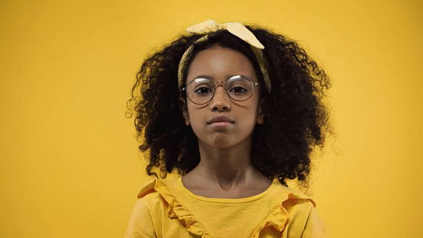 rizado africano americano chica en gafas mirando cámara aislada en amarillo - Foto, imagen