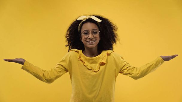 happy african american girl with outstretched hands isolated on yellow - Фото, изображение