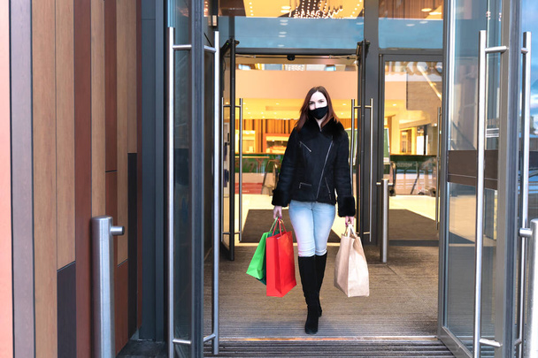 Mulher bonita em máscara protetora com sacos de compras sai shopping. Menina comprador elegante - Foto, Imagem
