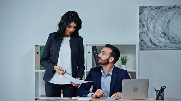 Empresária segurando papel perto de colega e laptop na mesa no escritório  - Foto, Imagem