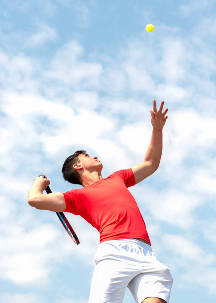 Leuke mannelijke tennisspeler in actie. Jonge tennisser tiener met racket raakt vliegende bal in sprong en blauwe hemel achtergrond. Competitieve sport spel, match. Verticale banner Kopieer ruimte - Foto, afbeelding