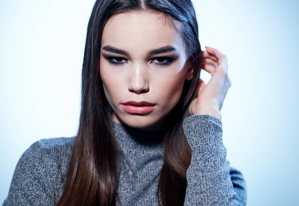 Hermosa modelo morena en suéter gris con maquillaje vista recortada sobre fondo claro - Foto, imagen