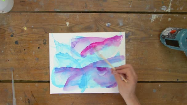Top view of artist paints an abstract picture, she uses paintbrush to paints abstract shapes with purple paint on wet canvas - Footage, Video