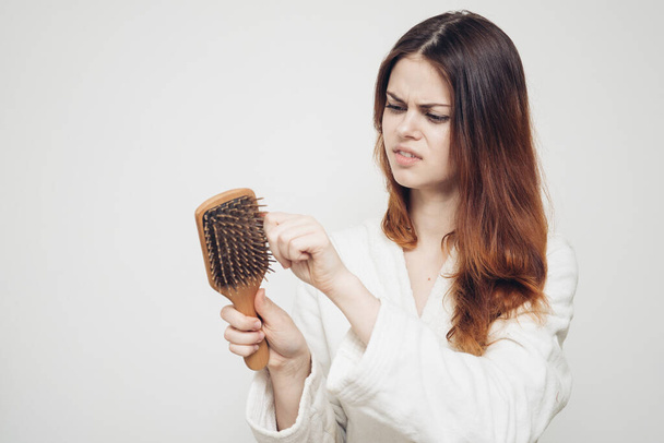 випадання волосся проблеми зі здоров'ям жінка з гребінцем в руці на світлому фоні
 - Фото, зображення