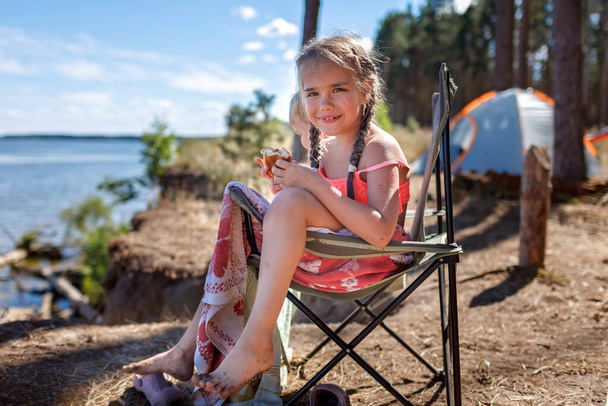 Kinderen zitten op een toeristische fauteuil, eten croissants en kijken naar zee tijdens een vakantie op de camping - Foto, afbeelding