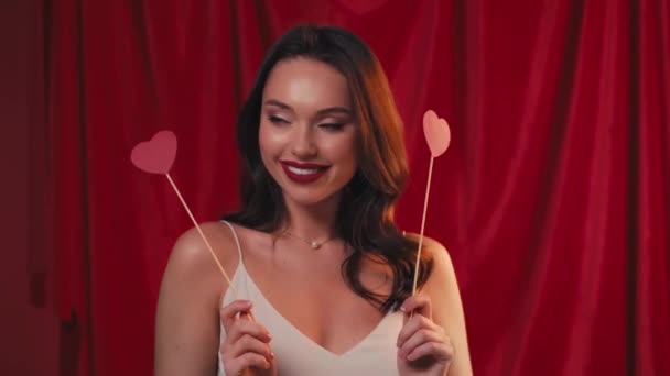 mujer alegre sosteniendo corazones en palos y sonriendo en rojo - Metraje, vídeo