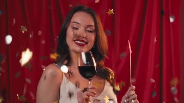 donna allegra che tiene il bicchiere di vino vicino a cadere coriandoli su rosso - Filmati, video