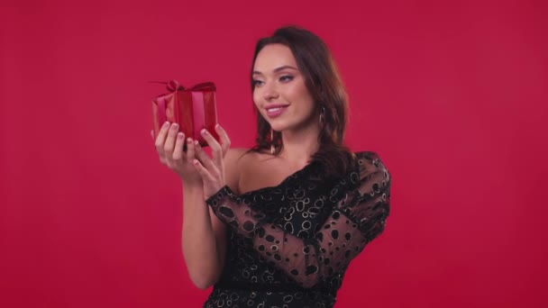 glückliche Frau im schwarzen Kleid hält Geschenk isoliert auf rot - Filmmaterial, Video