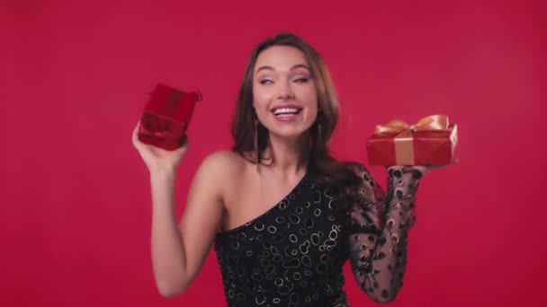 szczęśliwy kobieta w czarny sukienka gospodarstwa prezenty izolowane na czerwono - Materiał filmowy, wideo