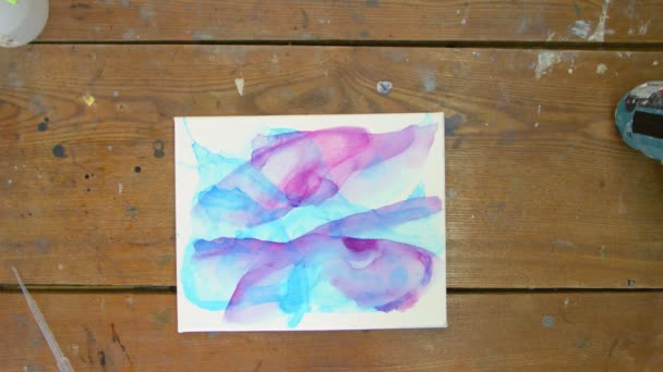 Top view a művész fest egy absztrakt képet, ő használ ecsetet festeni absztrakt formák lila festék nedves vászonra - Felvétel, videó