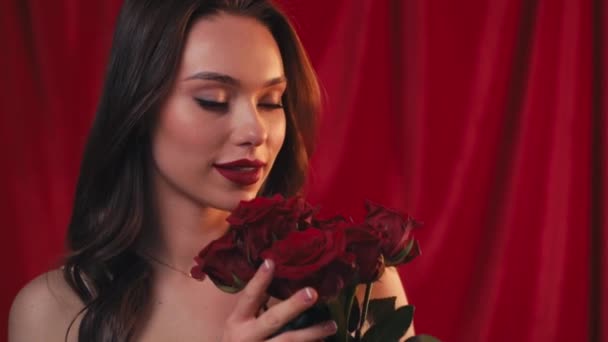 щаслива брюнетка жінка тримає і пахне трояндами на червоному
 - Кадри, відео