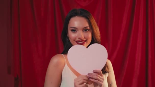 χαρούμενη γυναίκα χαμογελώντας και κρατώντας χάρτινη καρδιά στο κόκκινο - Πλάνα, βίντεο
