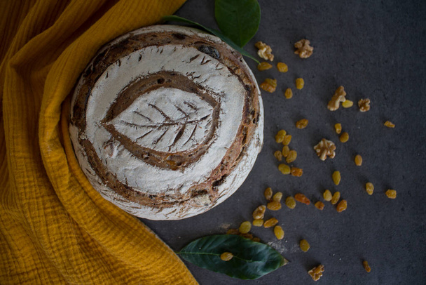 Beautiful rye sourdough bread on a table. Homemade bread made of whole grain. Healthy living concept. Crusty bread on a yellow kitchen towel. Top view photo of fresh baked sourdough bread. - Fotó, kép