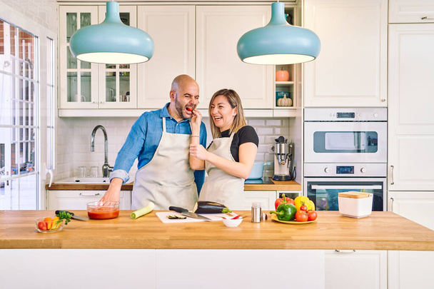 Ein glückliches junges Paar genießt und bereitet eine gesunde Mahlzeit zu. Sie bietet ihm eine Tomate an. Kochen zu zweit - Foto, Bild
