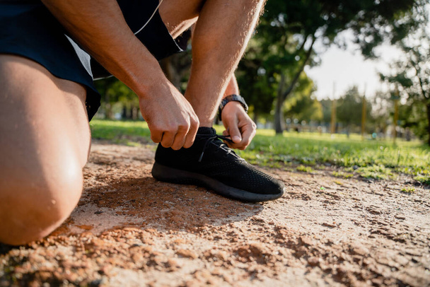 Jeune athlète masculin penchant vers le bas attachant des chaussures de course avant l'exercice sur le chemin de course en plein air - Photo, image