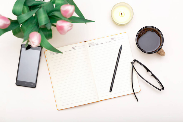 Λευκό άνετο χώρο εργασίας με σημειωματάριο, τηλέφωνο, καφέ, λουλούδια. Παραγωγική backgound τρόπο ζωής - Φωτογραφία, εικόνα
