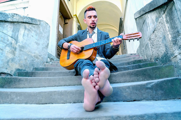 Male street musician playing guitar outdoors with bare feet in old European city.  Art and music concept.  - Photo, Image