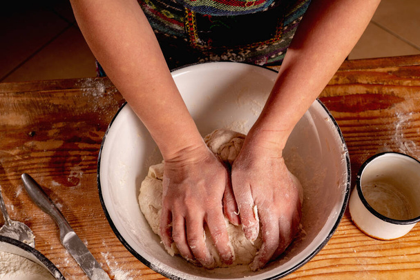 Πάνω όψη του γυναικείου φούρναρη προετοιμάζει τη ζύμη για το ψήσιμο σε ξύλινο τραπέζι κουζίνας. Επιλεκτική εστίαση στα χέρια. - Φωτογραφία, εικόνα