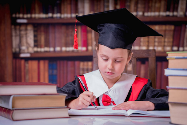 Красива молода школярка в шапці для випускників у галузі бібліотечного виробництва та написання плану освіти на майбутнє
. - Фото, зображення