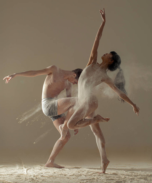 Two ballet dancers perform dance on the floor covered flour against background of white flour cloud in air. - Photo, Image