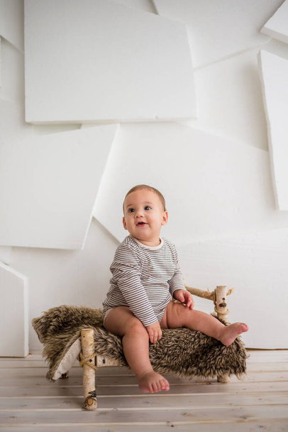 un bambino felice con un body a righe si siede su un lettino di legno su sfondo bianco - Foto, immagini