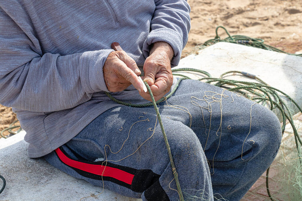 Руки рыбака чинят сеть ножом. - Фото, изображение