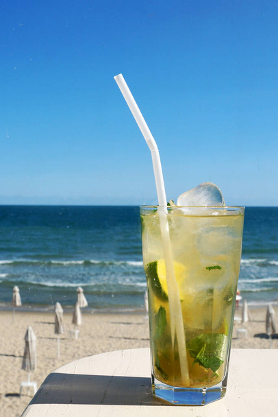 mojito cocktail with ice in a glass with a straw on the background of the sunny sea horizon. - Photo, Image