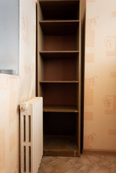 小さなキッチンの内側からのクローズアップ:錆びた中央暖房ラジエーターと収納棚。修理工事の準備. - 写真・画像