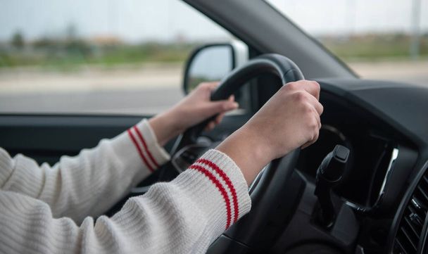 Nahaufnahme der Hände einer Person, die das Lenkrad eines Autos während der Fahrt auf einer Straße hält. - Foto, Bild