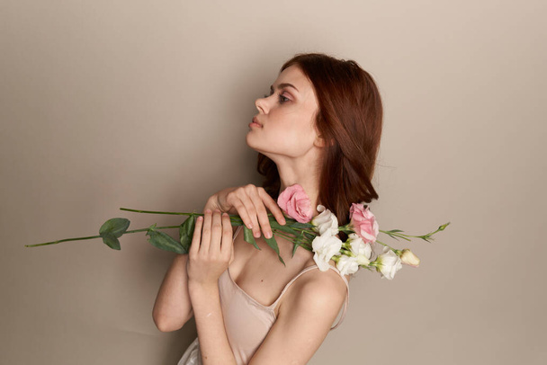 Glückliche Frau mit einem Strauß heller Blumen auf beigem Hintergrund nackte Schultern Modell rote Haare schönes Gesicht - Foto, Bild
