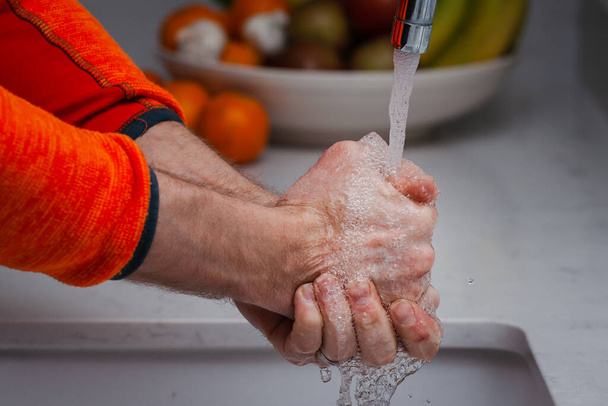 Мужчина моет руки под проточной водой из-под крана. Мужчина моет руки с мылом в раковине на кухне. - Фото, изображение