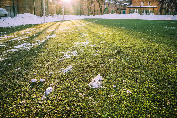 Πεδίο ποδοσφαίρου καθαρό από χιόνι. Το χιόνι βρίσκεται στην άκρη του γηπέδου ποδοσφαίρου σε μια τσουλήθρα. Ηλιόλουστη μέρα - Φωτογραφία, εικόνα