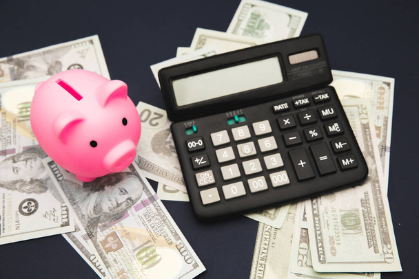 Бизнес, финансы, инвестиции, сбережения и коррупция концепция - крупным планом долларов наличными деньгами, калькулятор и розовый копилку на столе - Фото, изображение