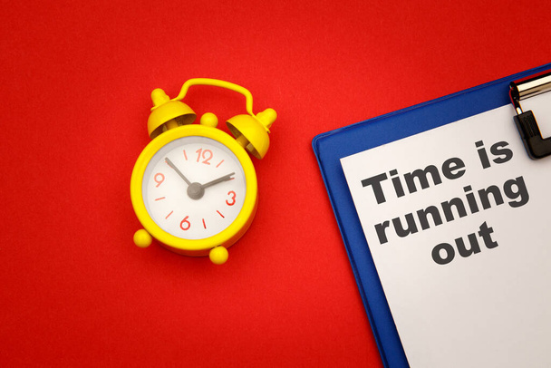Time is Running Out - phrase on paper with yellow alarm clock aside on red background - Photo, Image