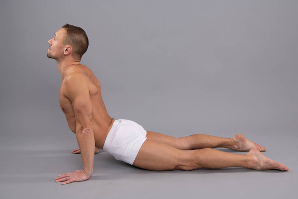 Yogi człowiek zrobić back-bending asana kobra joga pozować szare tło, pozycja ciała. - Zdjęcie, obraz