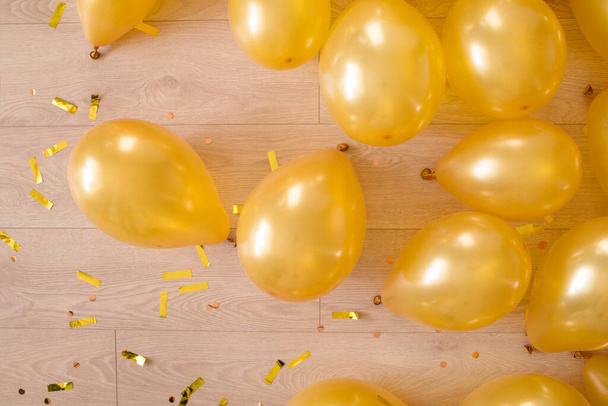 złote balony i konfetti na drewnianej podłodze. przygotowanie na urodziny lub inne przyjęcie. - Zdjęcie, obraz