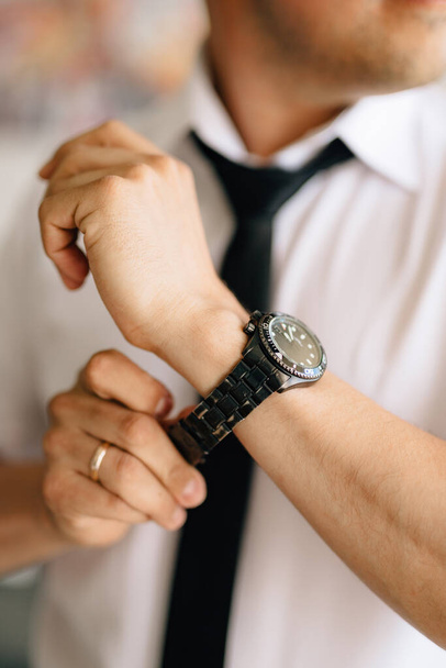 Мужчина в белой рубашке и галстуке надевает часы на руку во время подготовки к свадьбе - Фото, изображение