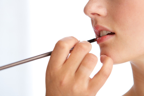 Mujer joven que aplica lápiz labial en los labios
 - Foto, imagen