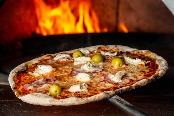 Restaurant chef neemt pizza uit de oven. Traditionele Italiaanse pizza bereiden. chef-kok met schop voor pizza, Italiaanse pizza wordt gekookt in een houtoven. - Foto, afbeelding