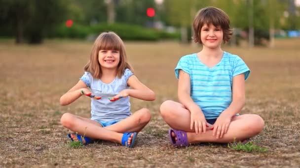 Dvě legrační sestry sedící na trávě se zkříženýma nohama a mávající malovanýma rukama v létě - Záběry, video