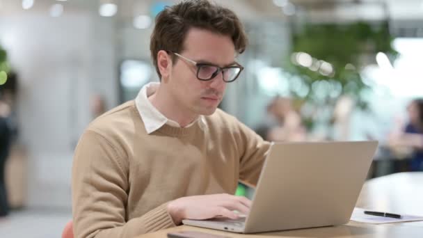 Молодой дизайнер работает над ноутбуком в офисе  - Кадры, видео