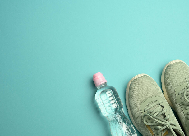 ζευγάρι αθλητικά sneakers και ένα μπουκάλι με μεταλλικό νερό σε μπλε φόντο, πάνω όψη, αντιγραφή χώρου - Φωτογραφία, εικόνα