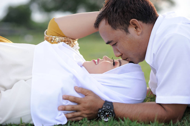 Муж и беременная жена, лежащие на траве, зашивают мужа, целуют его жену в лоб. Пара мусульманских фото материнства. Веселье в траве - Фото, изображение