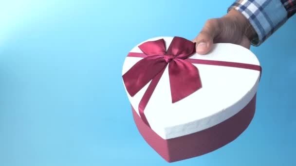 мужчина рука держит сердце формы подарочная коробка на голубом фоне  - Кадры, видео