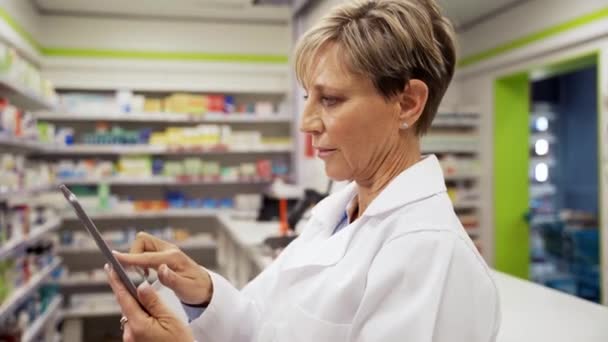Farmacista caucasica femminile che scorre su tablet digitale alla ricerca di prescrizioni per i clienti in farmacia  - Filmati, video