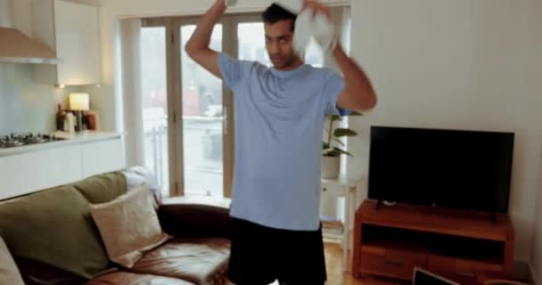 Смешанный спортсмен улыбается после тренировки в гостиной, держа в руках потное полотенце - Кадры, видео
