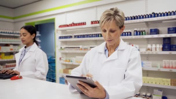 Caucasian pharmacist scrolling through scripts on digital tablet standing at counter in pharmacy. - Footage, Video